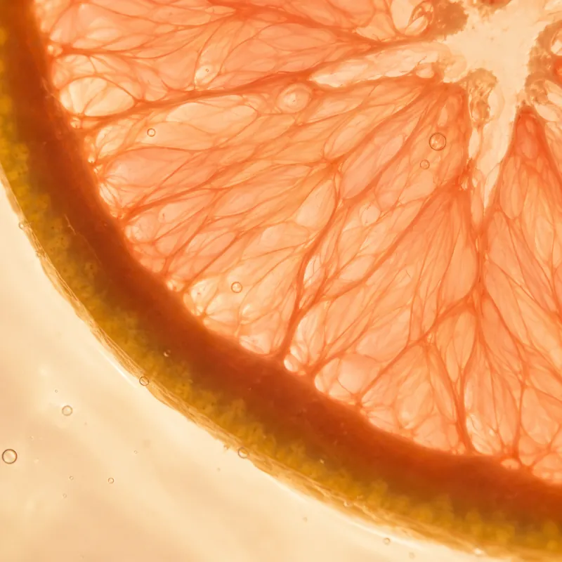 A close view of a backlit grapefruit slice with small bubbles in water.