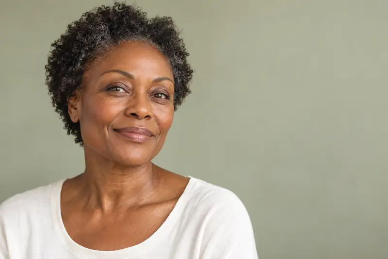 A woman in her fifties with short grey-black curls, smiling in daylight. Illustrative image for RF microneedling at LUMEN, Birmingham.